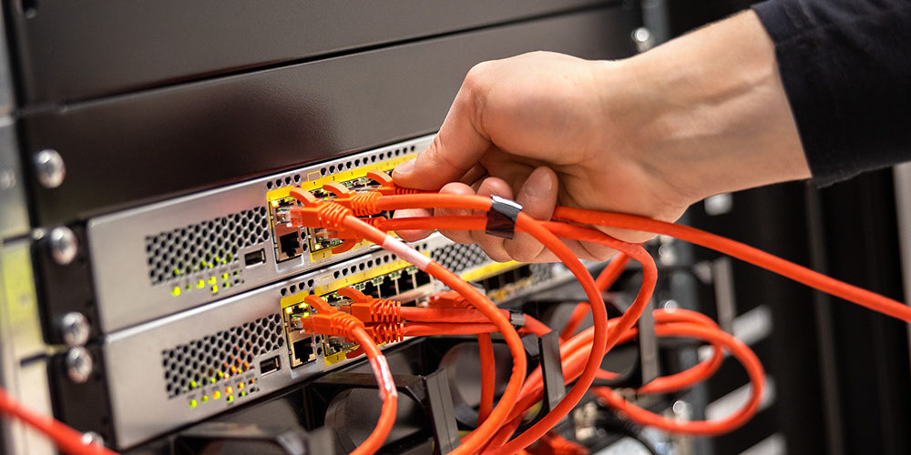 Cropped hand of male technician plugging network cable in router cluster at datacenter